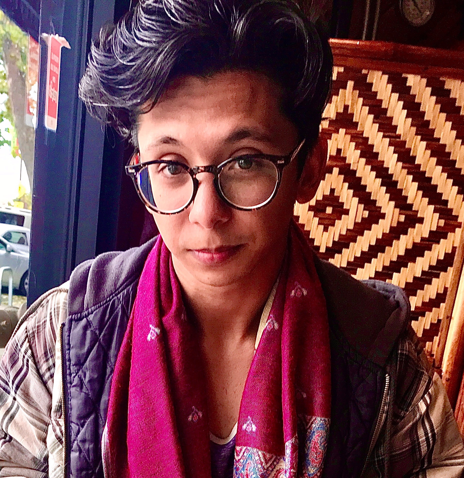 Picture of Manuel with a pink scarf and glasses and a geometric pattern on the chair behind them.